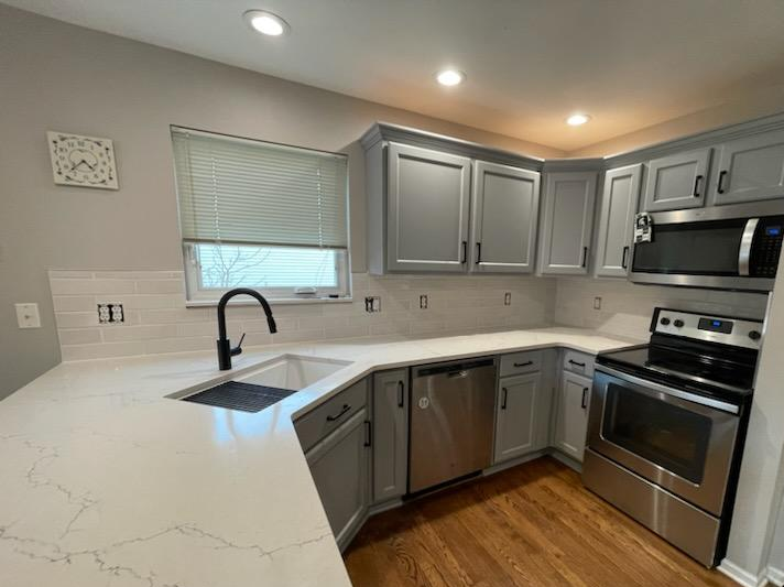 Gray kitchen cabinets with white countertops, stainless steel appliances and wood flooring